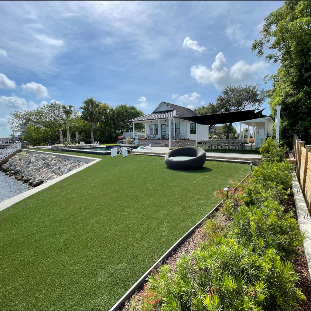 Waterfront property with artificial turf, landscaped edges, and shaded seating area in Galveston, TX.