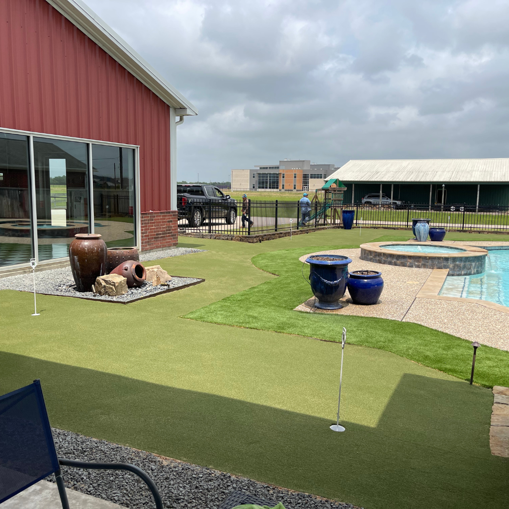 Custom backyard putting green installation surrounding a swimming pool, providing a varied and challenging putting experience, with decorative urns and gravel accents, installed by Sermons Turf Installs.