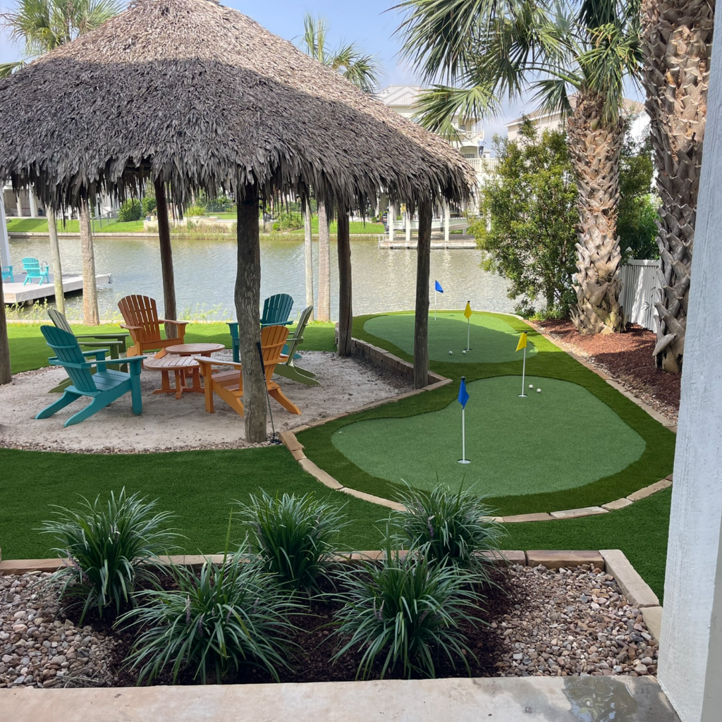 Two putting greens by Sermons Turf Installs near Galveston Bay, with a tiki hut installation, Adirondack chairs, and hammocks overlooking the water.