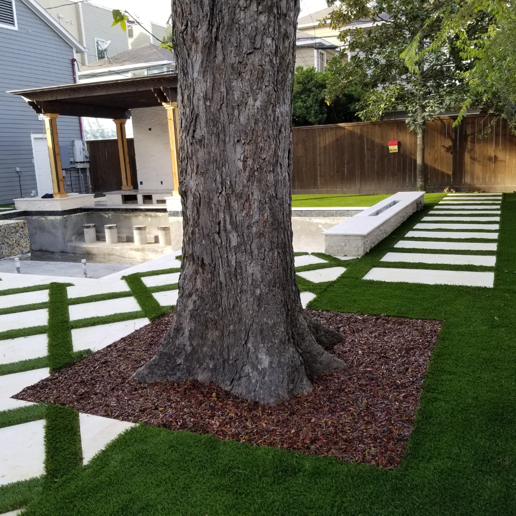 Outdoor space featuring custom pavers and artificial turf around a large tree.